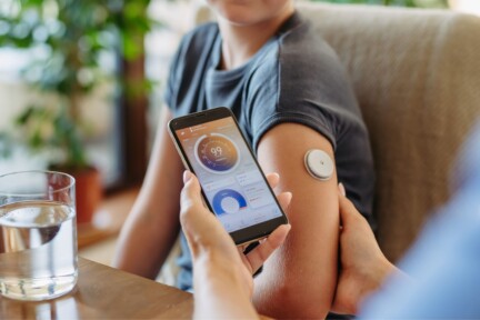 A caregiver uses a smartphone app to check glucose levels from a sensor on a child's upper arm.